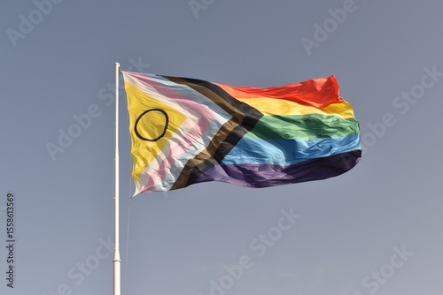 Intersex‑inclusive Progress Pride flag waving against a clear blue sky, symbolizing diversity and inclusion.