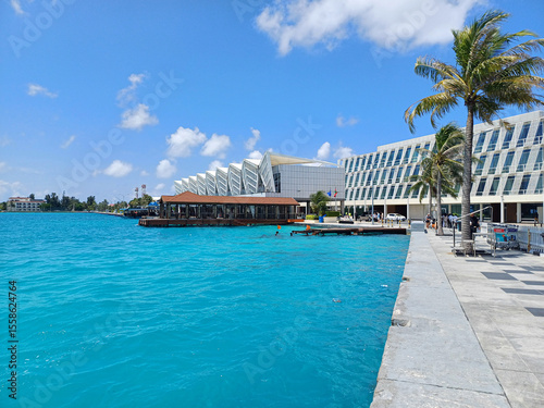 Waterfront scene at Velana International Airport features an expanse of turquoise blue water bordered by a concrete promenade, representing a tropical travel destination with unparalleled beauty