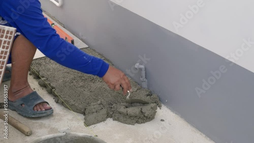 Hand carefully lays a white tile on gray mortar for home flooring, with another tile already set in position. The shot highlights the meticulous work of floor installation.