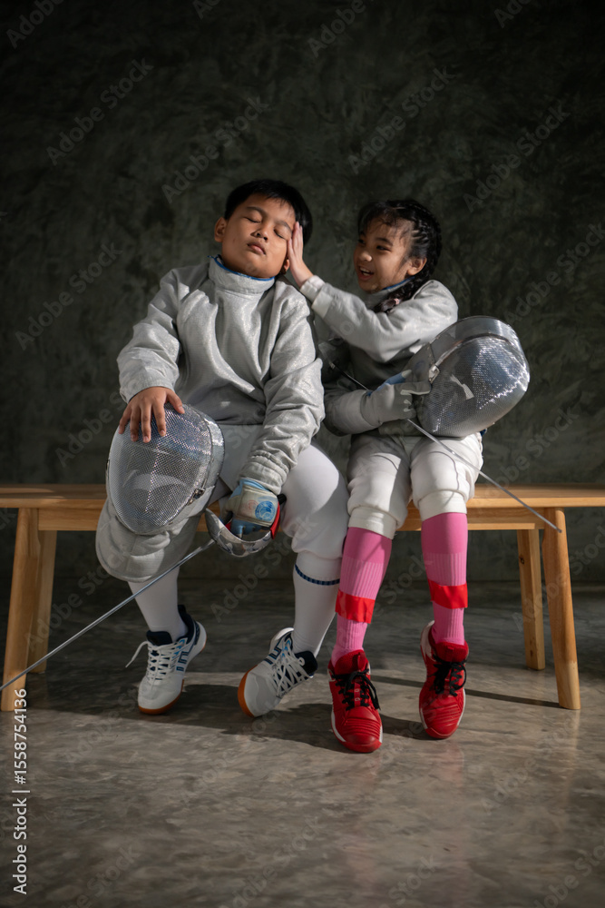 Obraz premium Two child in fencing gear sit on a bench, smiling at each other