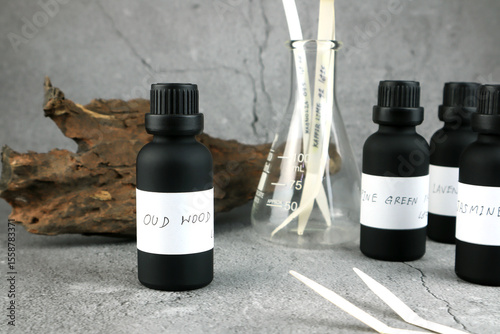 black color essential oil bottle is on white table with blotting paper , fragrance bottle and digital scale are used to blend the nice scent for making perfume and candle by perfumer in laboratory