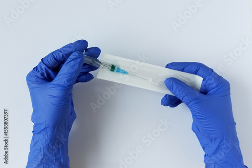 Hands with blue medical gloves. Takes out a syringe from a vacuum package. White background