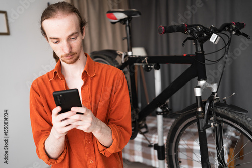 Young hipster man repairing bicycle using smartphone at home. Bicycle maintenance
