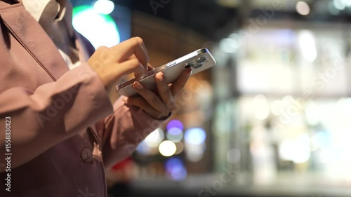 A close-up of a woman using a smartphone with a blank white screen at night. Technology, communication, and digital interaction in a modern urban setting.