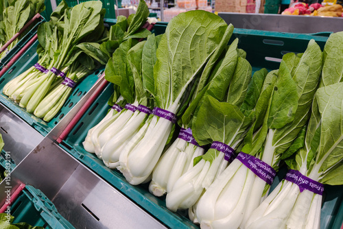 Fresh bundles of bok choy neatly arranged in a green plastic crate at a supermarket produce section, with visible white stalks and crisp green leaves8