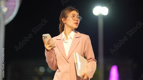 Young Asian woman standing taking notes professional working indoors with focus and confidence, managing digital work and business communication efficiently.