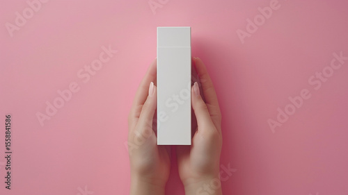 Young female hands holding blank white squeeze bottle plastic tube on pink background. Packaging of cream, lotion, gel, facial foam or skincare. Cosmetic beauty product branding mockup. Copy space.