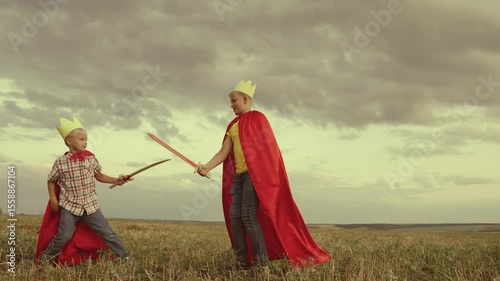 Boys brothers play red raincoats field. happy family. Children dream boys protect. victors, sword hand, fight while playing. happy family concept. children games park. boy golden crown park. kid play