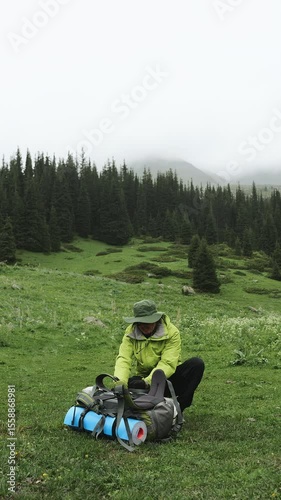 A tourist man in a green jacket prepares a backpack for a hike in the mountains. Professional tourist equipment. Vertical video.