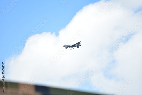 A drone flies in a blue sky with white clouds, viewed from a low angle.
