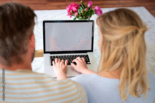 Rear view of a couple sitting on sofa and using a laptop computer