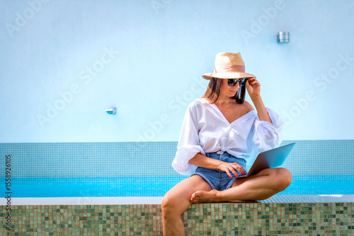 A woman sitting on the edge of the pool using a laptop