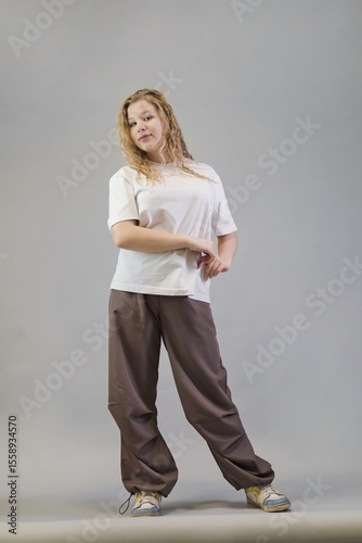 Seated in a relaxed pose, a woman in casual streetwear stretches her arms forward, dressed in a white t-shirt, black denim jacket, and beige pants. This image reflects the modern trend of effortless
