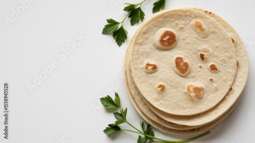 A close up shot of a stack of tortillas with parsley on a white background, top right corner