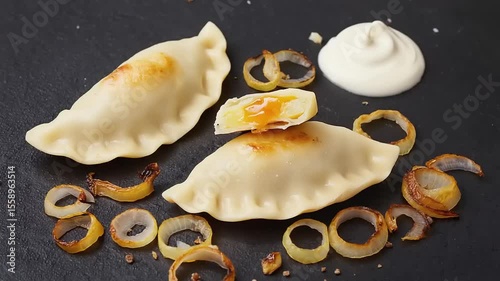 Pierogi with caramelized onions, and sour cream, on a dark plate