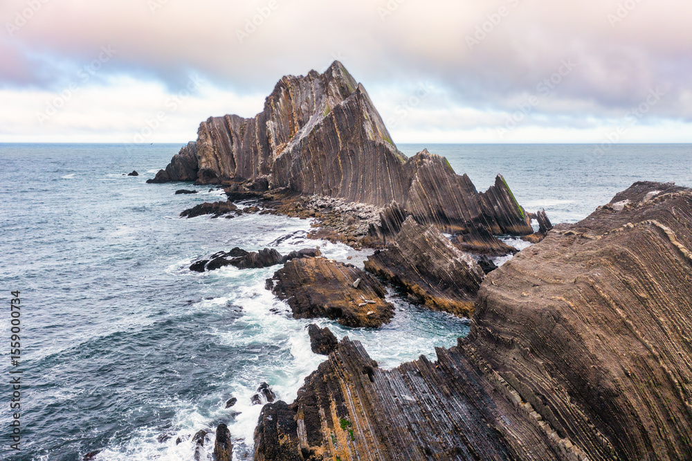 Obraz premium Aerial view of San Pedro Rock off the California coast near Pacifica. Sharp striated cliffs rise from the Pacific Ocean, Rugged texture, sea birds, and misty atmosphere create a wild coastal scene