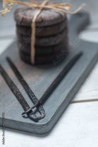 Close up studio still life photo with soft light and muted colors featuring dried vanilla beans on a vintage wooden board  with espresso and cookies in the background