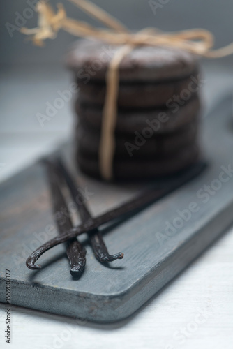 Close up studio still life photo with soft light and muted colors featuring dried vanilla beans on a vintage wooden board  with espresso and cookies in the background