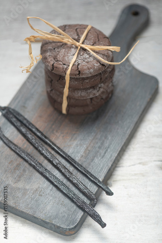 Close up studio still life photo with soft light and muted colors featuring dried vanilla beans on a vintage wooden board  with espresso and cookies in the background,  ideal for culinary