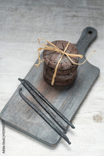 Close up studio still life photo with soft light and muted colors featuring dried vanilla beans on a vintage wooden board  with espresso and cookies in the background