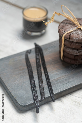 Close up studio still life photo with soft light and muted colors featuring dried vanilla beans on a vintage wooden board  with espresso and cookies in the background
