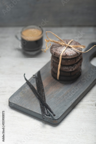 Close up studio still life photo with soft light and muted colors featuring dried vanilla beans on a vintage wooden board  with espresso and cookies in the background