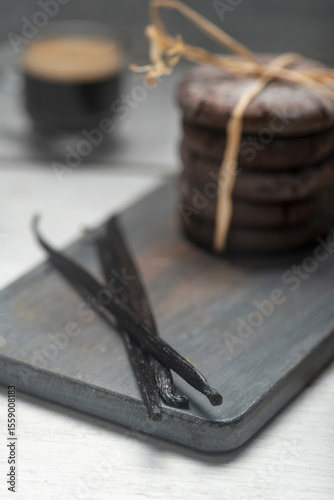 Close up studio still life photo with soft light and muted colors featuring dried vanilla beans on a vintage wooden board  with espresso and cookies in the background, 