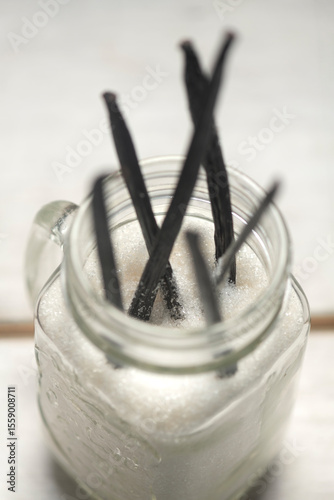 Close up studio photo of vanilla pods in glass jar in granulated sugar