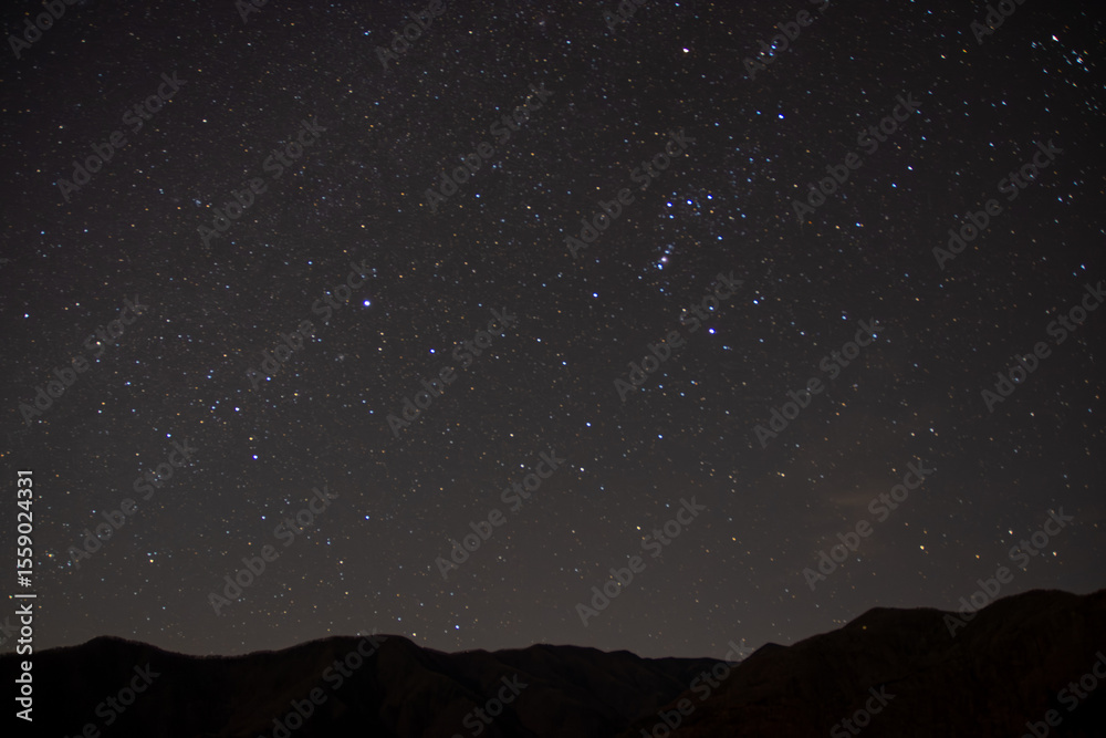 Obraz premium 埼玉県秩父市の山並みに浮かぶ冬の夜空と星空、オリオン座が輝く静寂な風景。澄んだ空気の中、山の稜線がシルエットとなり、自然と宇宙の神秘を感じさせる夜の風景。