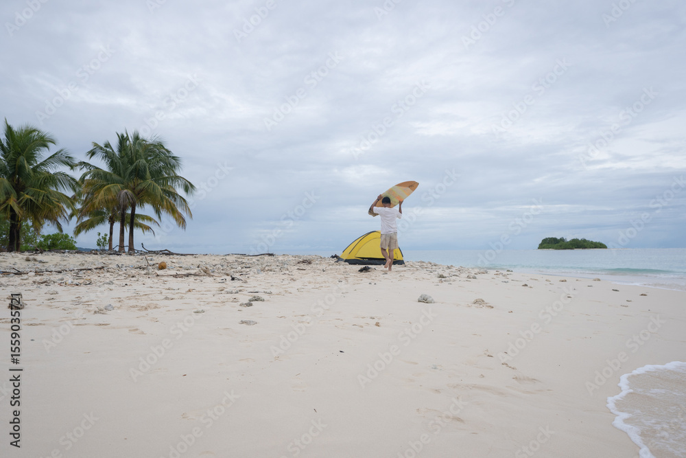 Obraz premium Aerial view of a surfer walks on a beautiful tropical beach carrying a surfboard. A male surfer walks alone on the beach