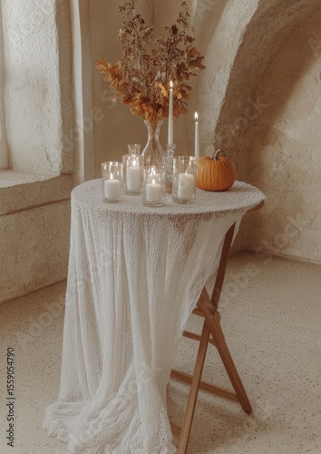 Cozy autumn table decor with candles, pumpkin, and dried flowers on white fabric