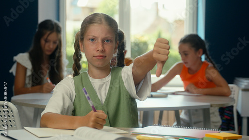 Caucasian teen sad girl displeased frowning kid child schoolgirl pupil student dissatisfied looking at camera education lesson studying problem disapprove bad fail thumb down dislike study in school