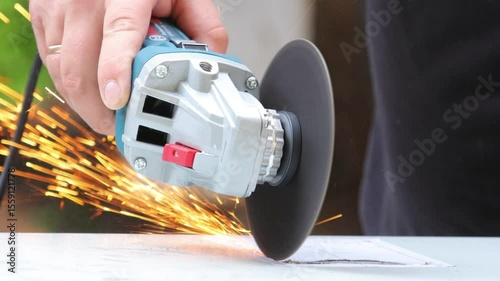Close-up of the hands of a metal craftsman making rectangular holes in a metal body with an angle grinder. Working with hand-held power tools in the workshop. Slow motion.