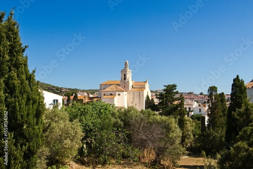 Charming narrow streets of Cadaqués, Spain, with white church on the hill, houses and vibrant blue sky, showcasing the historic Mediterranean coastal town’s beauty and traditional architecture