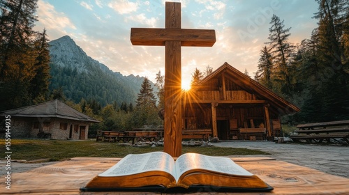 Wooden cross, open Bible, mountain chapel at sunset