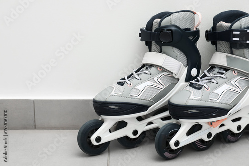 Fototapeta Naklejka Na Ścianę i Meble -  Pair of roller skates on floor near white wall, closeup. Space for text