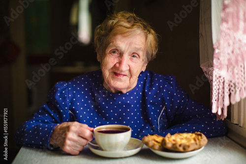 An elderly woman peacefully drinks tea in her home, her face calm and content. The portrait captures a gentle, warm moment filled with comfort, simplicity, and quiet joy.