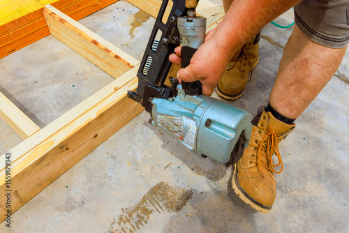 Worker is focused on using nail gun to secure wooden beams to floor in construction zone