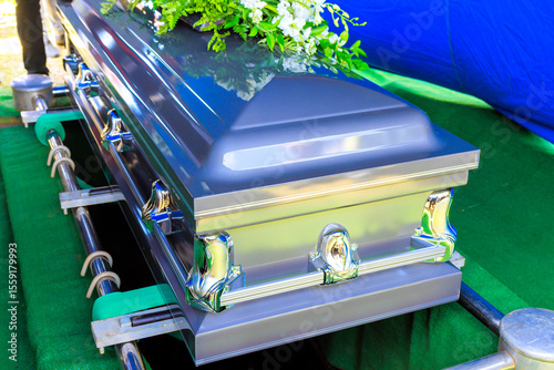 Family, friends gather around flower adorned coffin during solemn burial funeral service in peaceful setting.