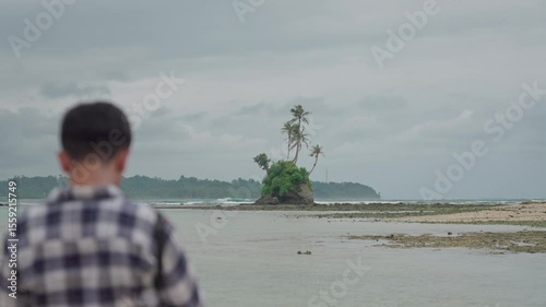 A man captures the beauty of Indonesia's tropical beaches on a sunny day. An aerial view shows a man standing and photographing a tropical beach