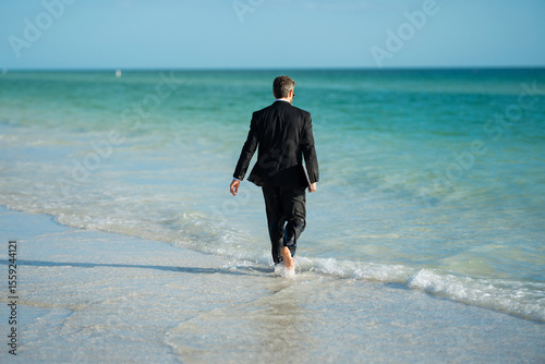 Leisure weekend and remote freelance work. Crazy comic business man in suit rest on sea bech. Rear view of back business man in suit in sea water at beach. Remote summer business. Summer holiday.