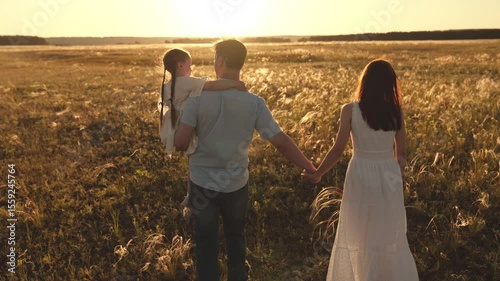 Father carries daughter blending with rustle of wind through ears of wheat. Father embraces held daughter and wife walks near wheat field. Father holds daughter in arms remained unwavering