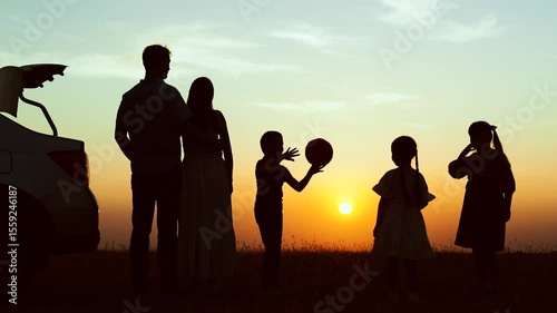 Silhouettes children parents at sunset near car in field. Family vacation in nature road trip picnic girls boys children kids parents dad mom in park. Journeys travelling road trip hiking picnic.