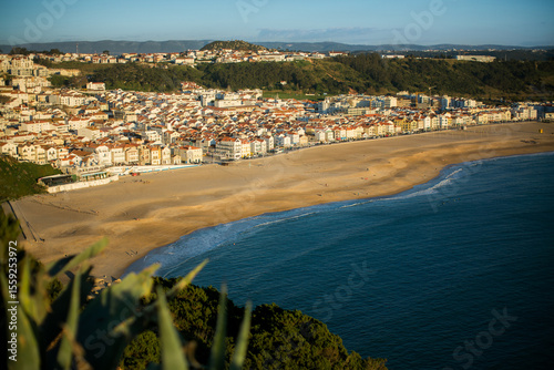 An ocean beach in Nazaré on a calm day, with gentle waves meeting the wide sandy shore. The peaceful atmosphere contrasts with the place’s famous wild surf, offering a moment of quiet and openness.