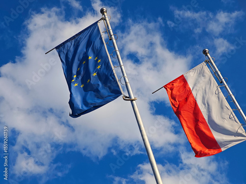 European Union and Polish Flags Together – Symbol of Unity and National Identity. European Union and Poland flags waving side by side against a bright sky.