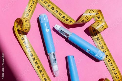 Two Ozempic injection pens with measuring tape on pink background. Concept of weight loss, diabetes treatment, and modern medicine. Two injectors dosing pens for subcutaneous injection