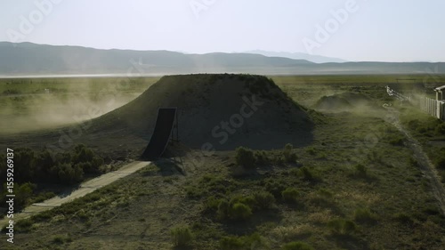 Professional motorcyclist leaping over large jump and onto mound - cinematic drone shot
