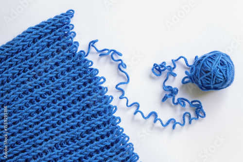 Unravelling blue wool knitted garment on white background. Copy space
