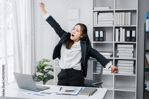 Tired Asian Businesswoman Stretching at Desk Overworked Young Professional Taking a Break from Work Long Hours Exhausted Female Yawning Office Stress Relief