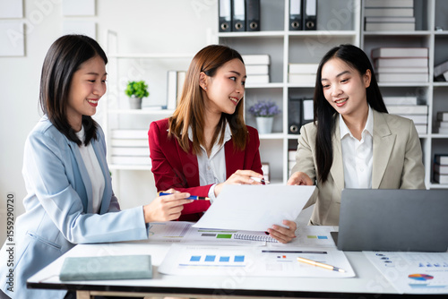 Three women are sitting at a table with a white piece of paper in front of them